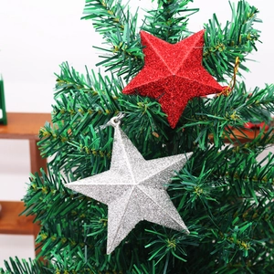Detail of red and silver glitter star ornaments hanging on green Christmas tree branches