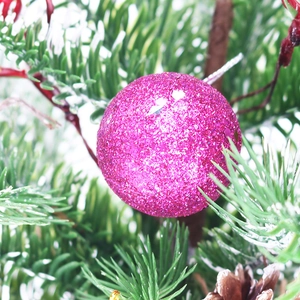 Close-up of pink glitter Christmas ball ornament hanging on a pine tree branch