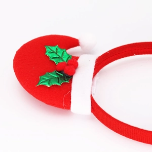 Detail of red velvet Christmas hat headband with green holly leaves and white plush pom-pom