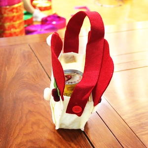 Close-up of felt Christmas gift bag with red handle and berry decor on wood table