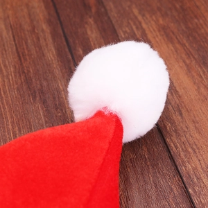 Dettaglio del cappello di Natale rosso in TNT con pompon bianco morbido su superficie in legno