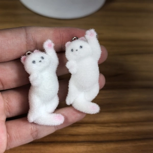 Close-up of white flocked cat charms with soft texture and pink details for DIY jewelry