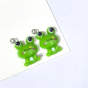Detalle macro de lindos colgantes de ranas de resina verde con anillas de plata para joyería
