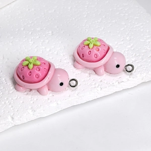 Close-up of two pink resin strawberry turtle pendants with silver metal loops for DIY