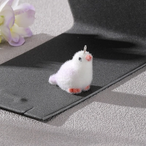 Macro shot of white flocked bird pendant with orange beak on a black display stand
