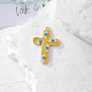 Dettaglio del ciondolo a croce dorata con smalto giallo e ciondoli a forma di occhio blu