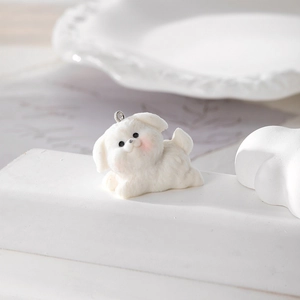 Close-up of a white flocked puppy pendant on a geometric stand for DIY jewelry making