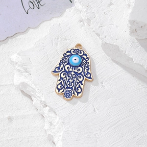 Dettaglio pendente Mano di Fatima dorata con malocchio blu su sfondo in pietra
