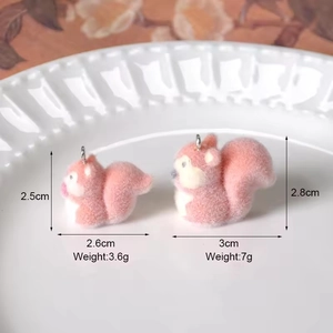 Pink flocked squirrel pendants in two sizes displayed on a white ceramic plate