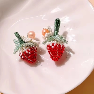 Detailed close-up of handmade beaded strawberry earrings with mini pearls and green stems