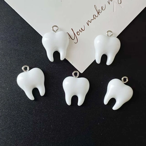 Close-up of five white resin tooth-shaped charms with metal loops for DIY jewelry making