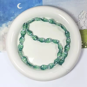 Dettaglio di perline di vetro fatte a mano a forma di pesce verde con motivi a onde bianche