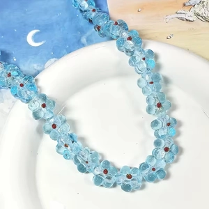 Gros plan de perles fleurs en verre bleu clair dans un plat blanc pour bijoux DIY