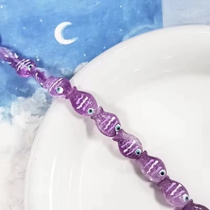 Dettaglio macro di perline di vetro viola a forma di pesce con strisce per gioielli DIY