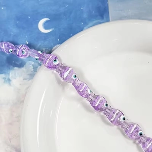 Dettaglio di perline viola a forma di pesce con occhio di Allah su piatto bianco