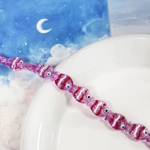 Dettaglio di una perla a forma di pesce rosa per gioielli fai-da-te su un piatto bianco