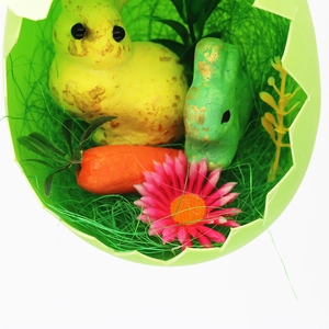 Close-up of Easter figurines with foam bunnies and carrot inside a green egg shell