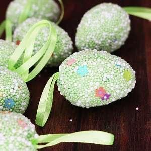 Close-up of light green foam Easter egg with colorful flower sequins and satin ribbon