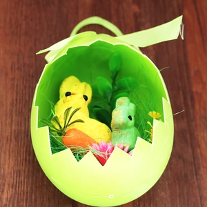 Top view of a green Easter egg gift basket with bunny figurines and carrots on wood