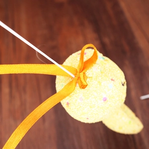 Close-up of yellow foam Easter egg ornament with orange ribbon bow on wooden background