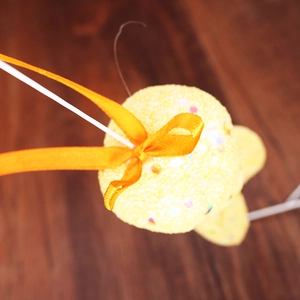 Close-up of a yellow sequined bunny foam egg ornament with a bright orange ribbon bow