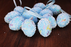 Close-up of blue foam Easter eggs with colorful sequins and hanging ribbons on wood