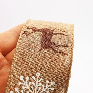 Macro detail of faux linen Christmas ribbon featuring golden reindeer and white snowflakes