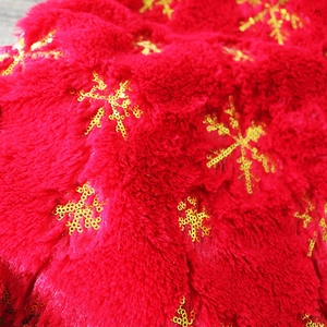 Dettaglio del tessuto peluche rosso con ricamo di fiocchi di neve in paillettes dorate