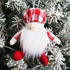 Gnome de Noël avec chapeau à carreaux rouges suspendu à un sapin enneigé en gros plan