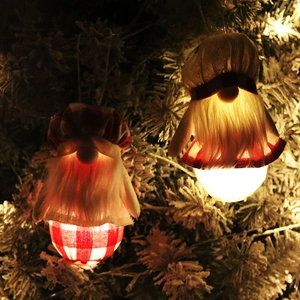 Gros plan de deux gnomes de Noël lumineux avec LED suspendus dans un sapin enneigé