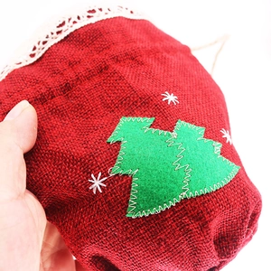Close-up of red burlap Christmas gift bag with embroidered tree and lace detail