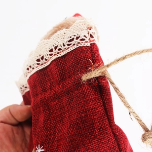 Close-up of red linen Christmas gift bag with white lace trim and rustic twine drawstring