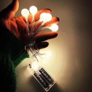 Detail of warm white LED globe string lights with transparent AA battery box held in hand