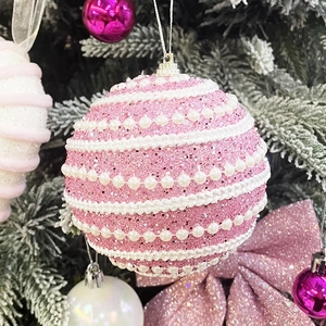 Boule de Noël rose avec paillettes, perles blanches et cordon argenté sur branche de sapin