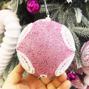 Boule de Noël rose avec dentelle blanche et paillettes sur branches enneigées