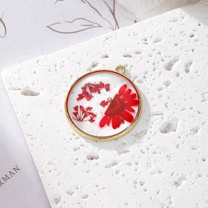Detail of round golden alloy pendant with red dried flowers and pearl in resin