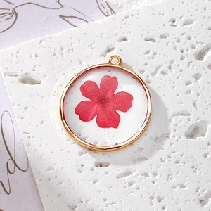 Gros plan d'un pendentif rond doré en résine avec une véritable fleur séchée rouge