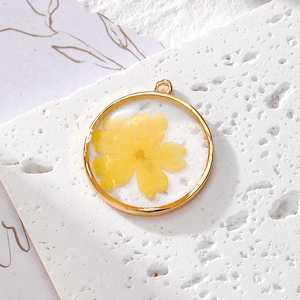 Gros plan d'un pendentif rond doré avec fleur séchée jaune en résine pour bijoux DIY