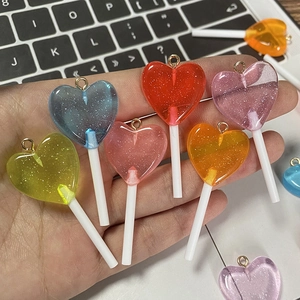 Handheld view of multi-colored glitter heart lollipop resin charms with golden loops