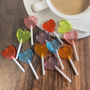 Macro shot of glitter resin heart lollipop charms with golden metal loops on wood
