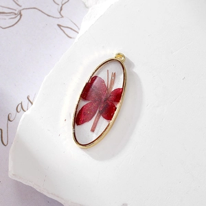 Macro detail of oval resin pendant with red dried flower and gold metal frame for DIY jewelry