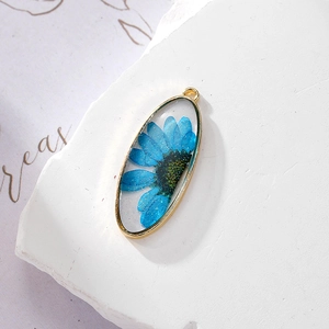 Oval gold pendant with blue dried daisy flowers and glitter inside clear resin
