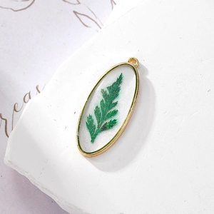 Detailed macro view of oval gold pendant with real fern leaf in resin and glitter