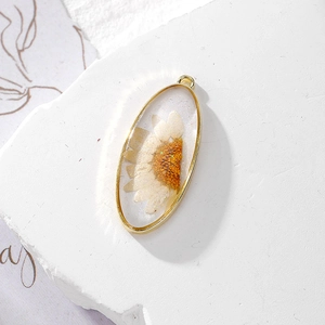 Detailed close-up of oval resin pendant with real white daisy flower and gold metal frame