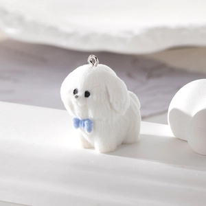 Dettaglio del ciondolo a forma di cucciolo floccato bianco con fiocco blu e gancio