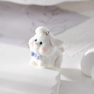Dettaglio di un ciondolo a cucciolo floccato bianco con fiocco blu 3D e anello in metallo