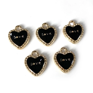 Detalle de dijes de corazón en esmalte negro con letras Love doradas y borde perlado