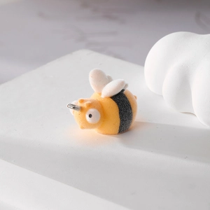 Macro shot of a yellow flocked bee charm with metal ring on a white stone pedestal