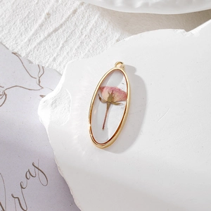 Detail of oval resin pendant featuring a real pink dried rose bud in a gold alloy frame