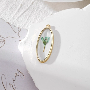 Detail of oval golden pendant featuring a real light blue dried flower in resin